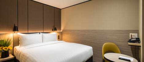 Une chambre d’hôtel moderne avec un lit bien fait, un petit bureau avec une chaise et un téléphone fixé au mur.