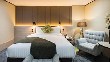A modern hotel room with a large bed, two bedside lamps, a side table, a chair, and a small round table.