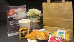 Un assortiment de petit-déjeuner comprenant un croissant, un muffin et un yaourt, un sac en papier et un panneau indiquant « Petit-déjeuner continental ».