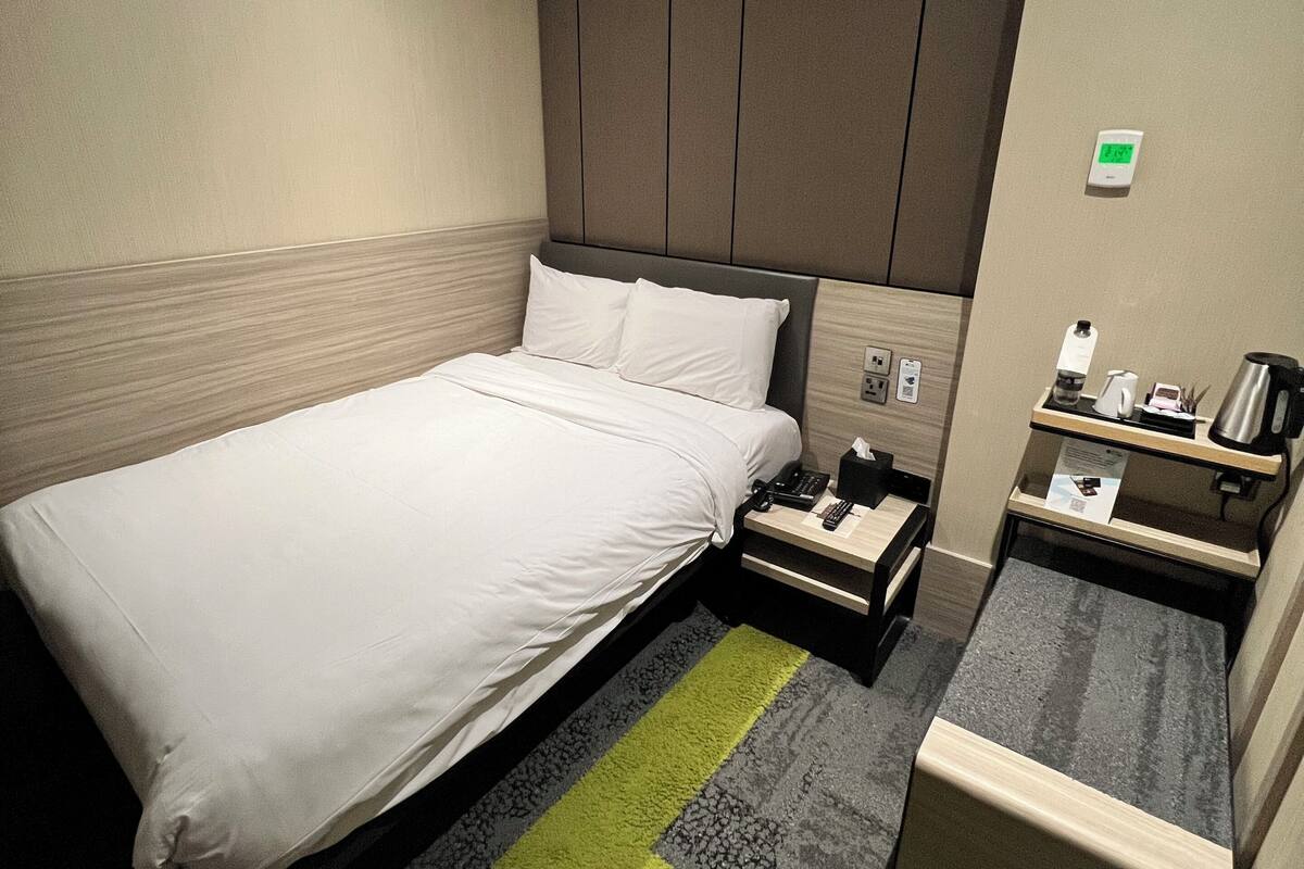A hotel room with a bed, bedside table, and a small desk with a chair.