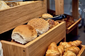 Una caja de madera para pan con diferentes tipos de pan, incluyendo bollos y croissants.