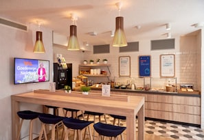 A modern kitchen area with a wooden counter, bar stools, and hanging pendant lights.
