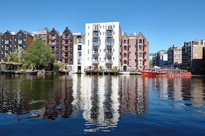 A canal with buildings on one side and a red boat on the water. - Holiday Inn Express Amsterdam - City Hall by IHG (Amsterdam)