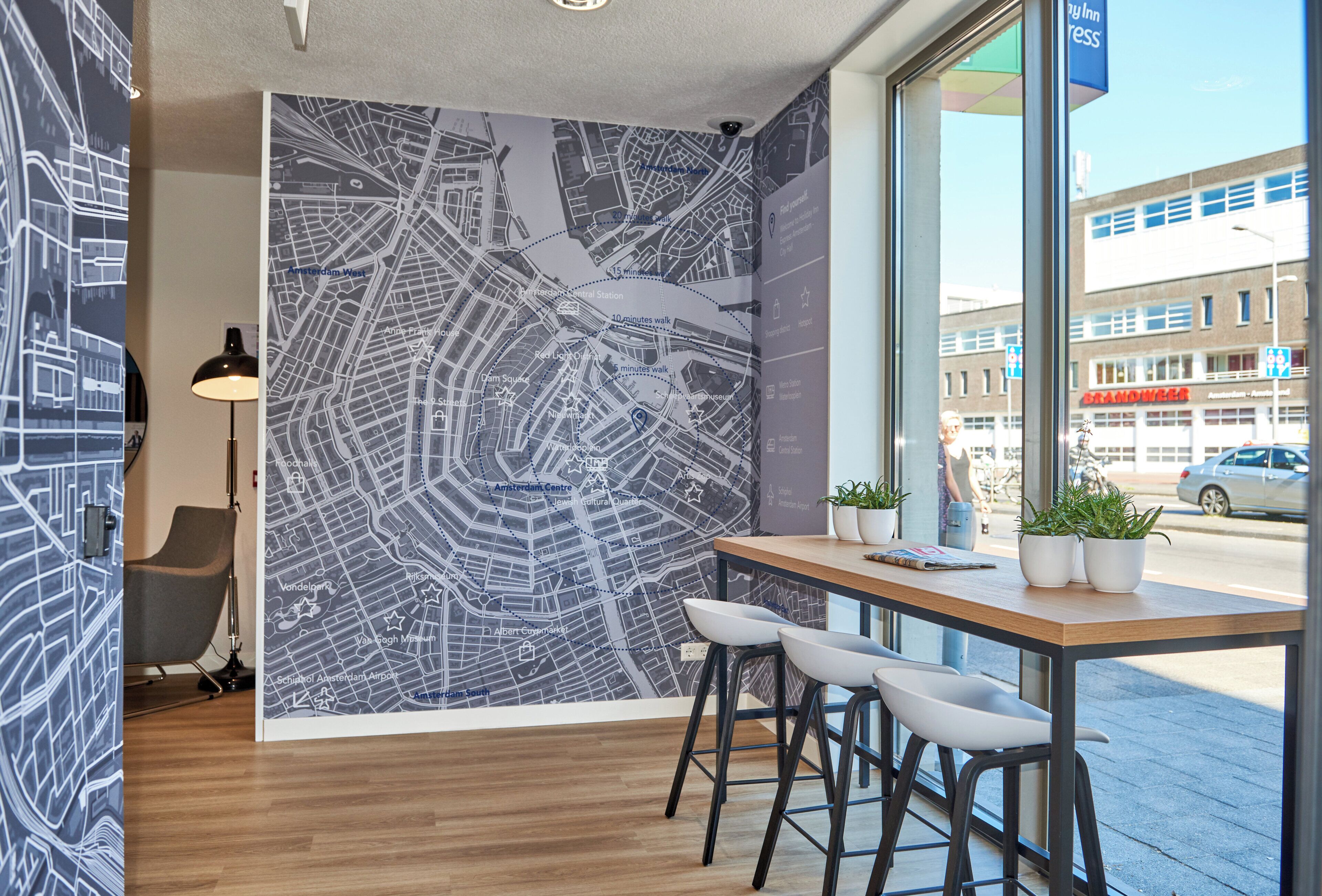 A modern interior with a large wall map, a wooden table, two white chairs, and a view of the street outside.