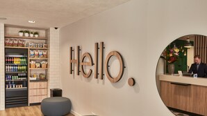 A reception area with a 'Hello' sign, a counter, seating, and a beverage display. - Holiday Inn Express Amsterdam - City Hall by IHG (Amsterdam)