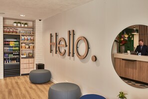 Zona de recepción con un cartel que dice 'Hello', mostrador, asientos y una exhibición de bebidas.