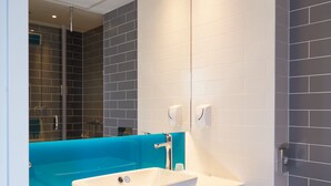 A modern bathroom with a large mirror, a white sink, a blue accent wall, and a glass shower enclosure. - Holiday Inn Express Amsterdam - City Hall by IHG (Amsterdam)