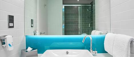A modern bathroom with a white sink, a blue accent wall, a glass shower enclosure, and a white towel on the right.