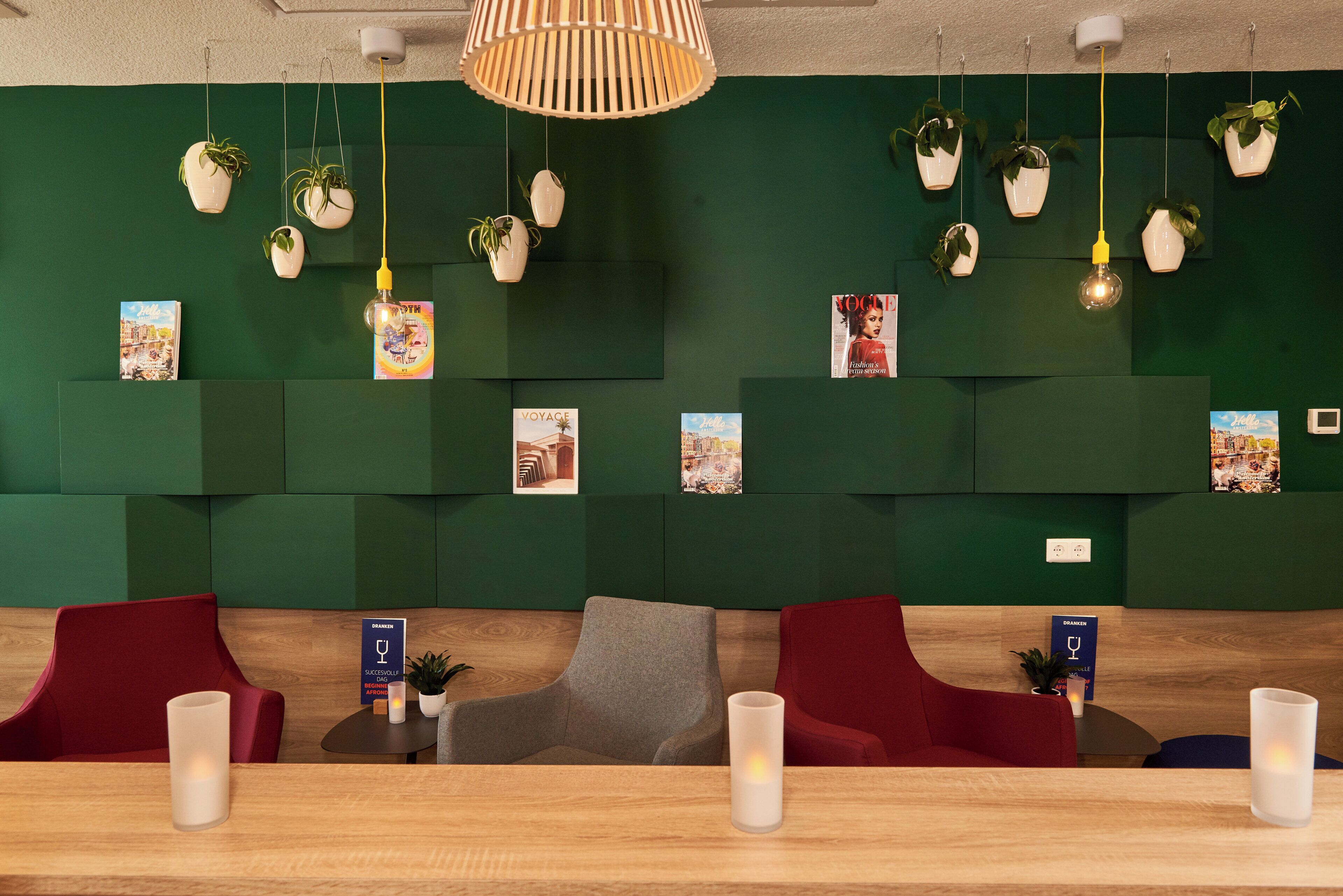 A reception area with green walls, multiple potted plants, magazines, and a wooden reception desk.