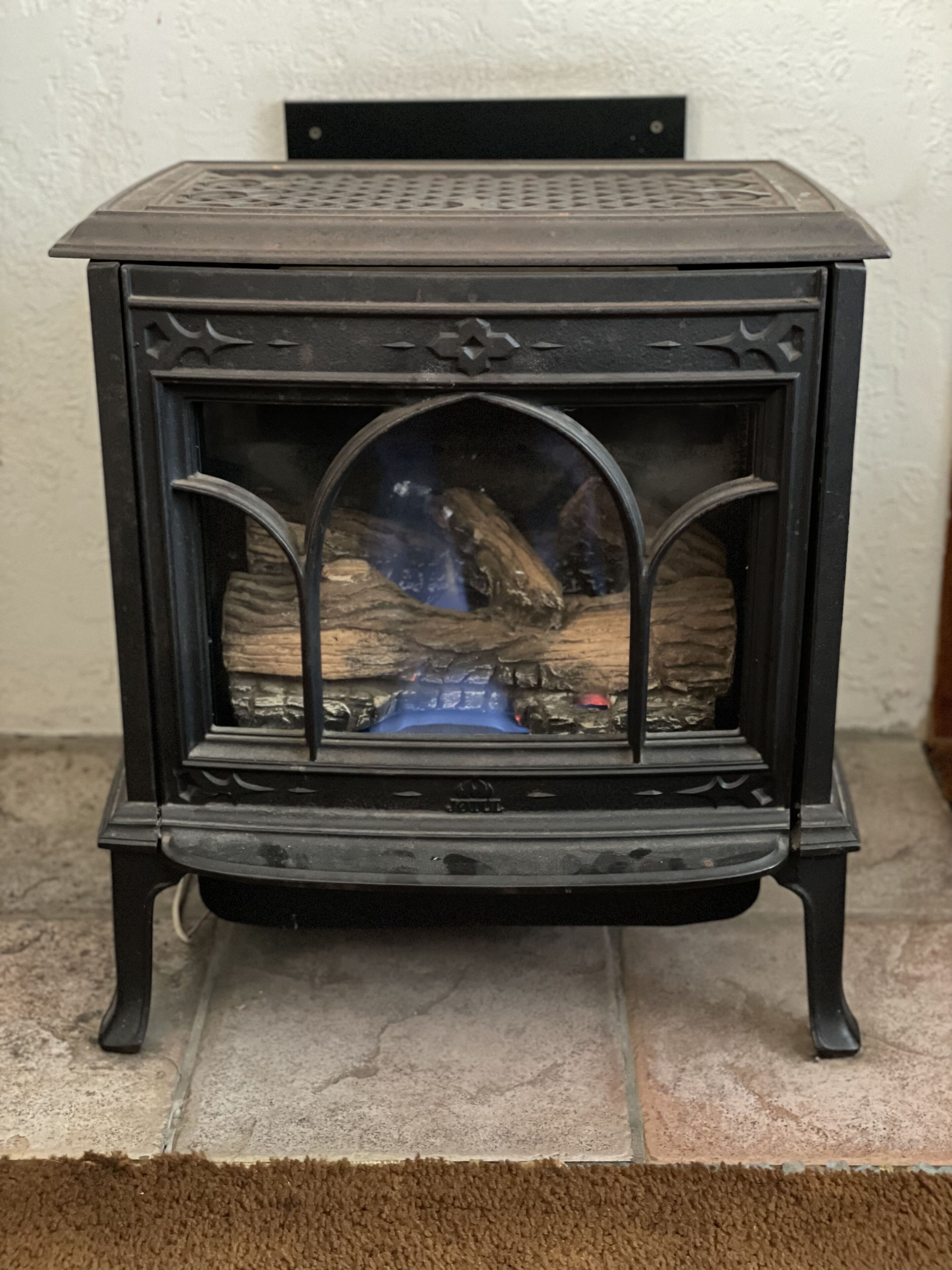 A black wood-burning stove with a glass front, placed on a tiled floor with a brown rug in front.