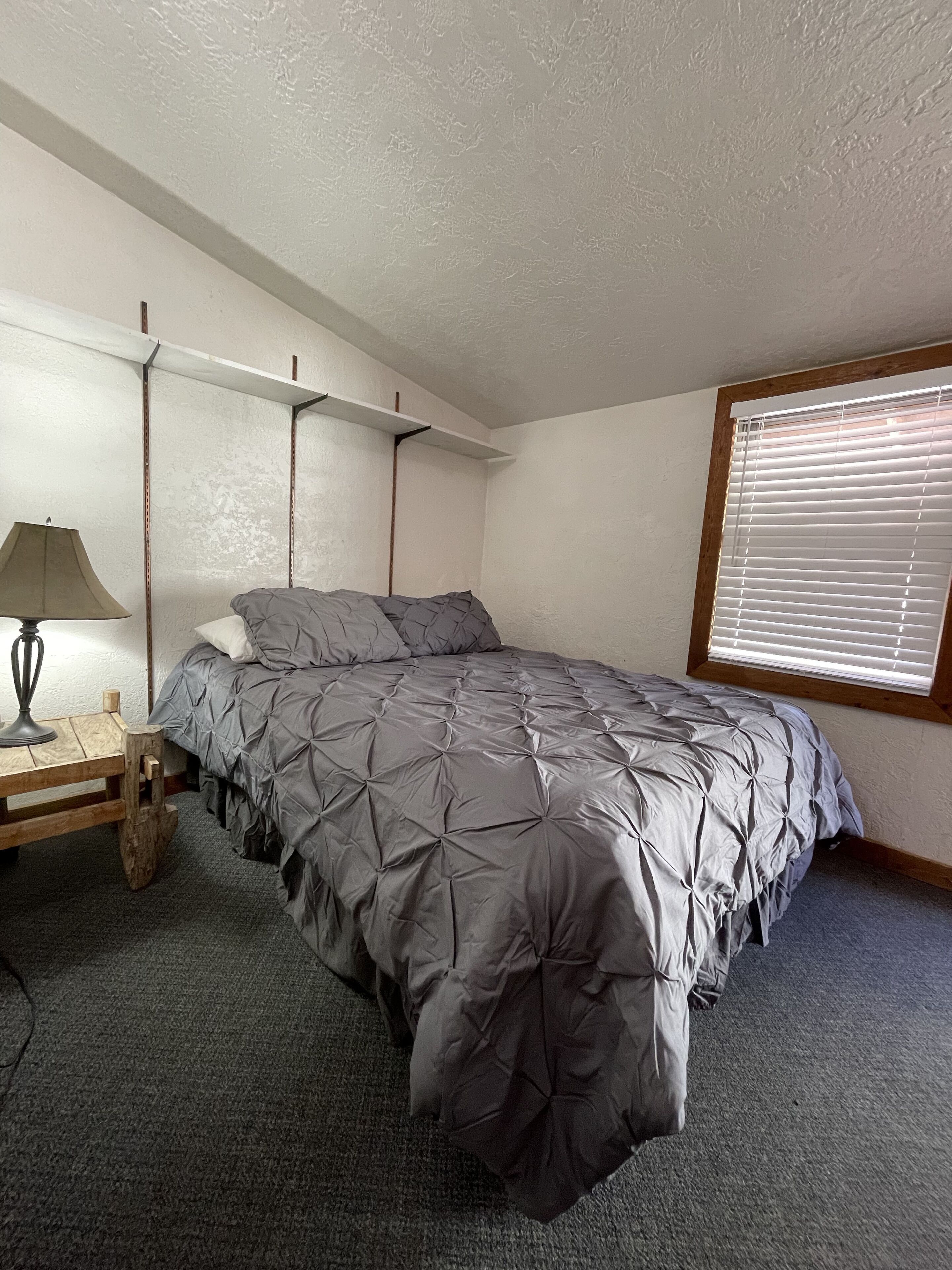 A bedroom with a bed, a nightstand, a lamp, and a window with blinds.