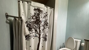 A bathroom with a shower curtain featuring a tree design, a toilet, and a wooden ceiling. - Adventures Vacation Rentals (Lava Hot Springs)