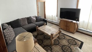 A living room with a sofa, a coffee table, a TV, and a patterned rug. - Adventures Vacation Rentals (Lava Hot Springs)