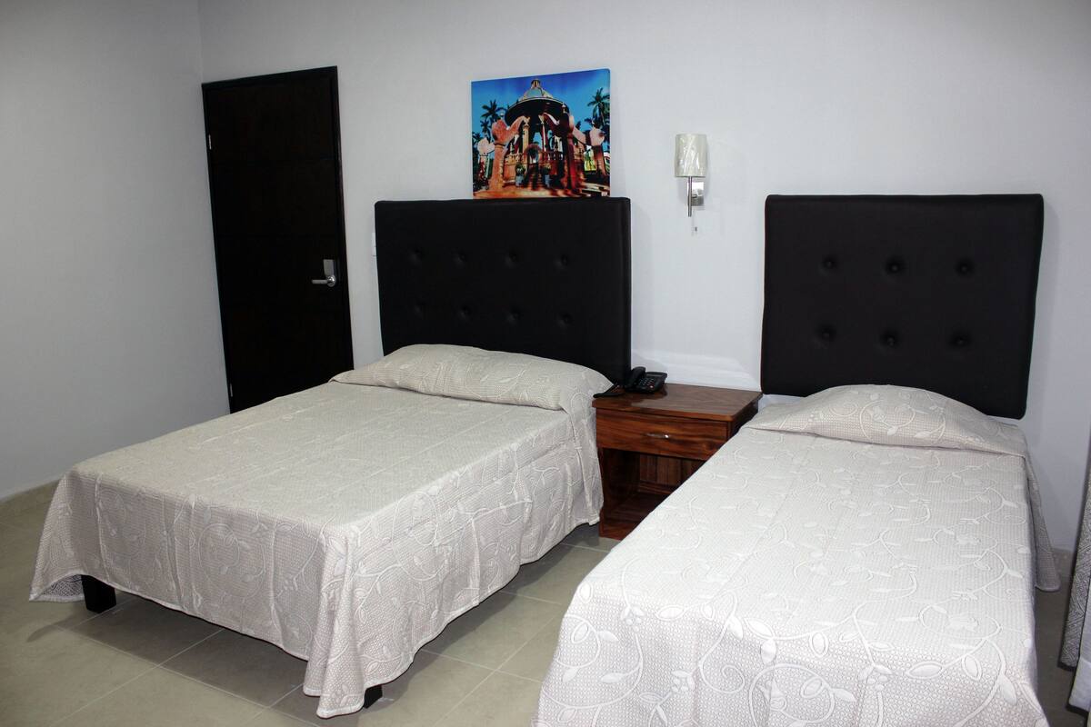 A room with two single beds, a wooden nightstand with a telephone, a wall-mounted light, and a door.