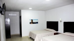 Habitación de hotel con dos camas individuales, un televisor de pantalla plana, una mesita y un cuadro de un edificio en la pared.