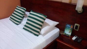 A hotel room with a neatly made bed, striped pillows, a wooden headboard, a nightstand with a remote control, and a brochure.