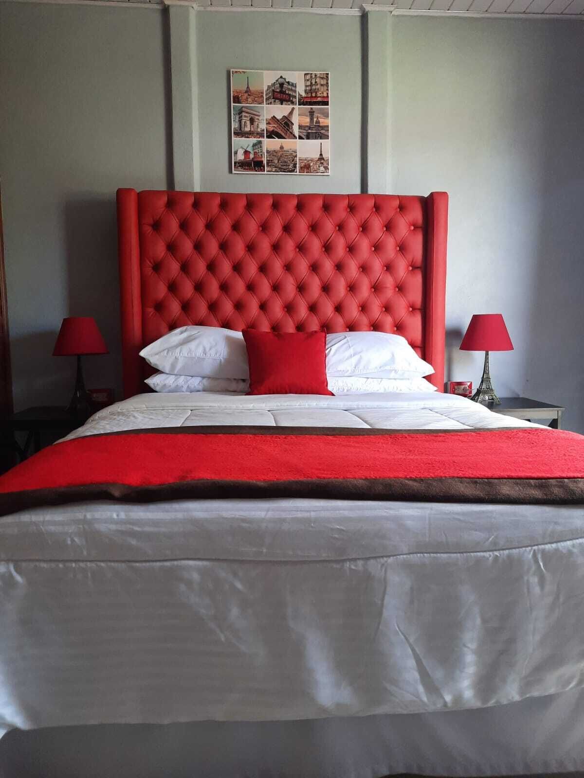 Un lit avec une tête de lit rouge, une literie blanche et des touches de couleur rouge. Deux lampes rouges sont placées de chaque côté du lit.