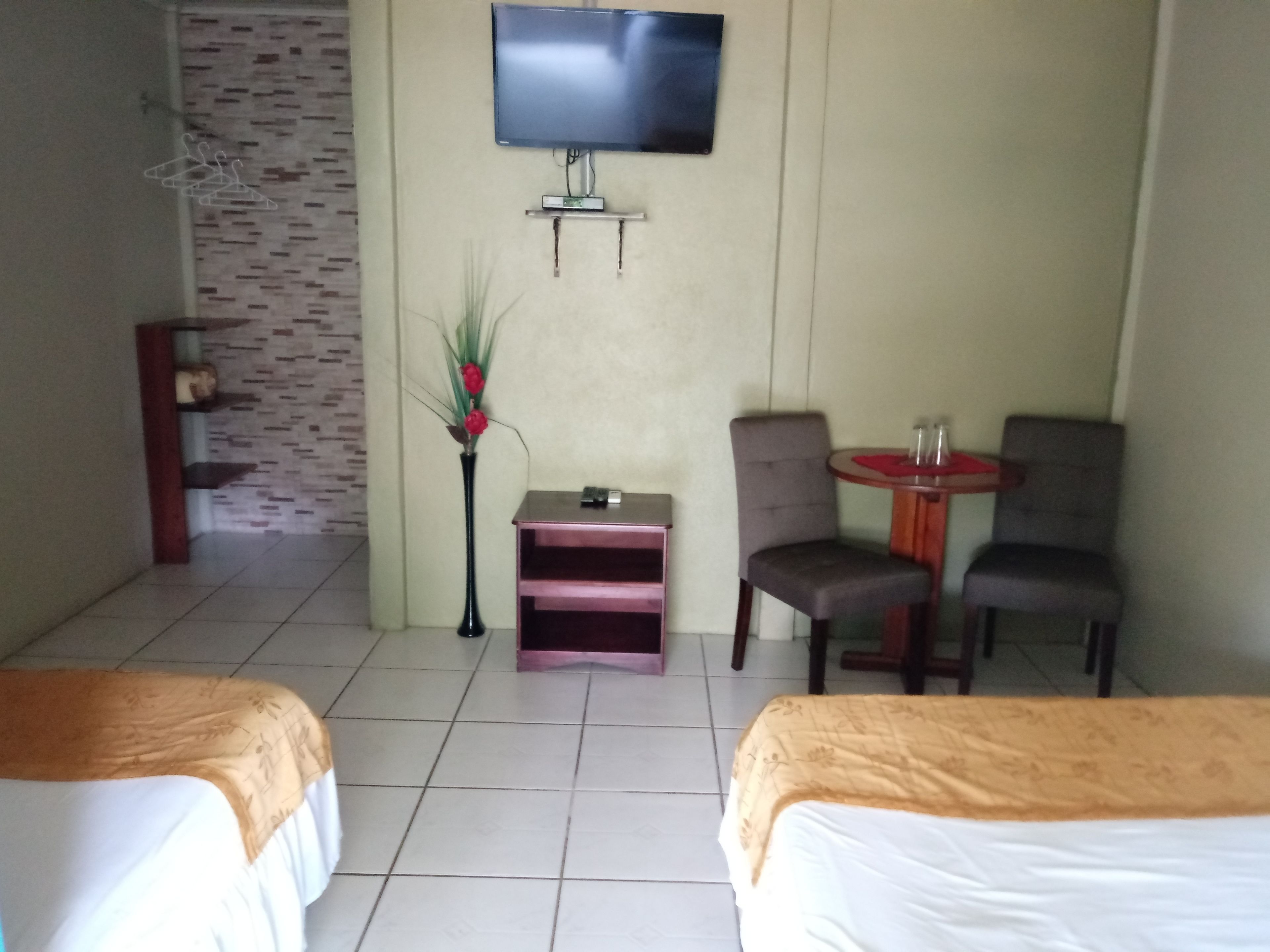 A hotel room with two beds, a TV mounted on the wall, a small table with chairs, and a decorative plant.