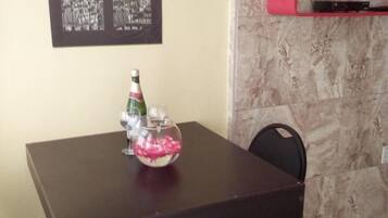 A dining table with a bottle and a bowl of pink items, a framed picture of the Eiffel Tower, a television on a red shelf, and a chair.