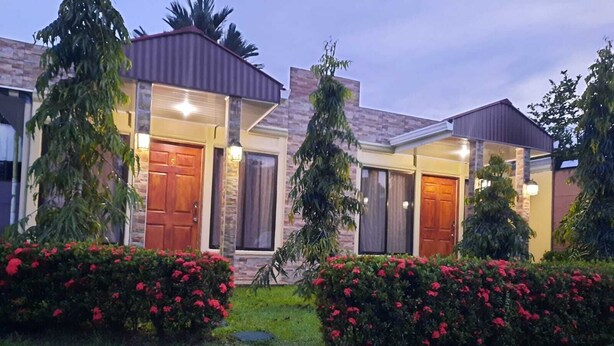 Una casa moderna de dos pisos con un jardín bien cuidado, con arbustos florecientes rojos y césped.