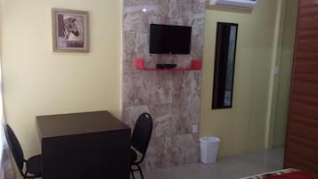 A small room with a table and chairs, a mounted TV, a trash bin, and a framed picture on the wall.