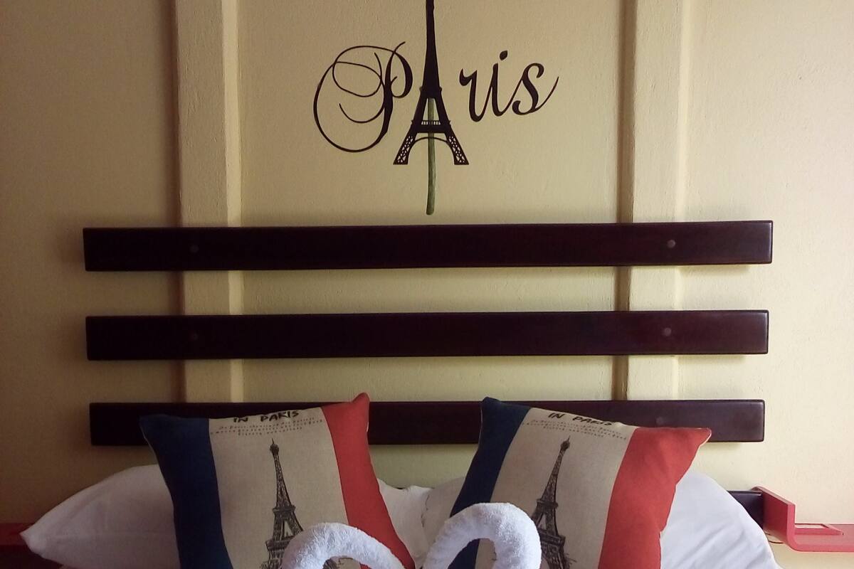 Une chambre d’hôtel avec un lit doté d’une tête de lit sur le thème de Paris, des oreillers ornés de motifs représentant la Tour Eiffel et un cygne décoratif fait de serviettes.