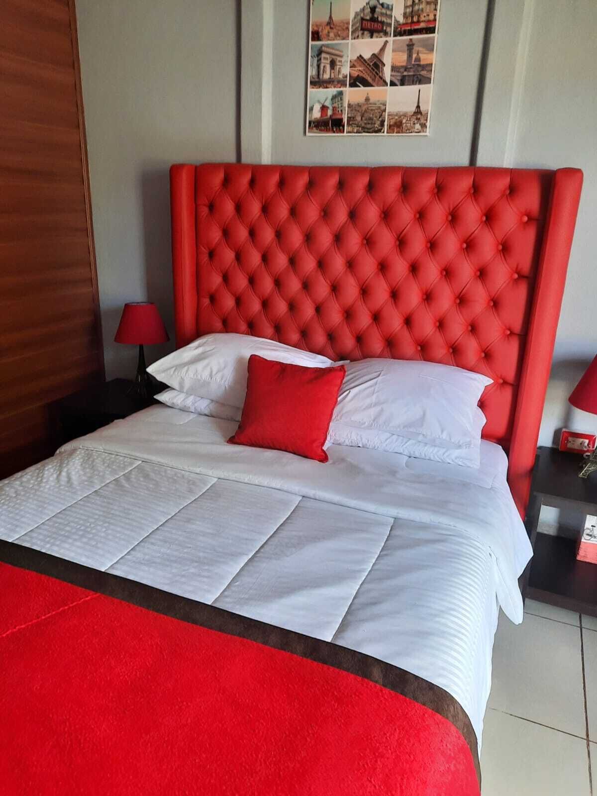 A hotel room with a large bed, red headboard, white bedding, and a red throw blanket.