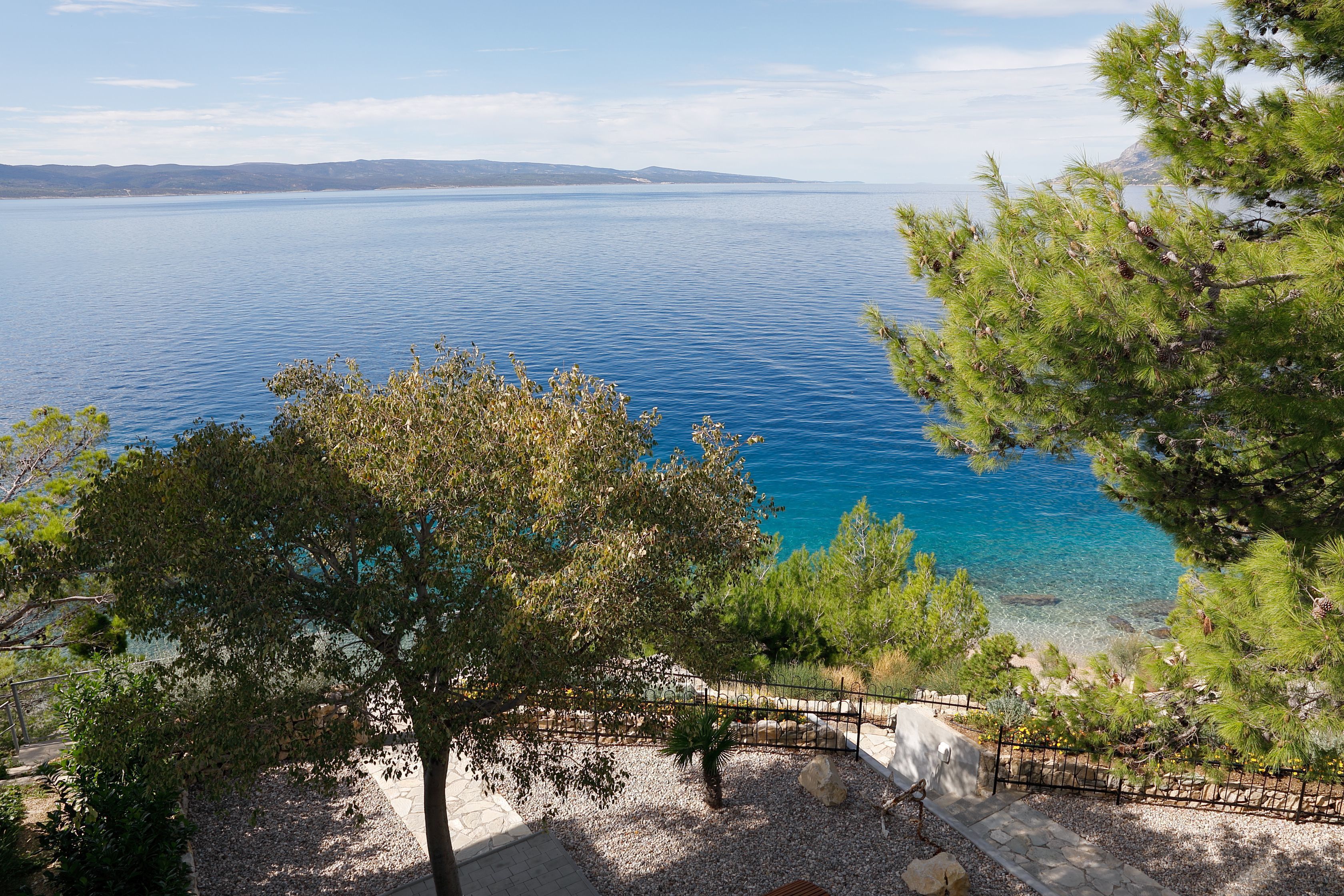 Une vue sur la côte, avec un ciel dégagé, une mer calme et une côte rocheuse bordée d’arbres.