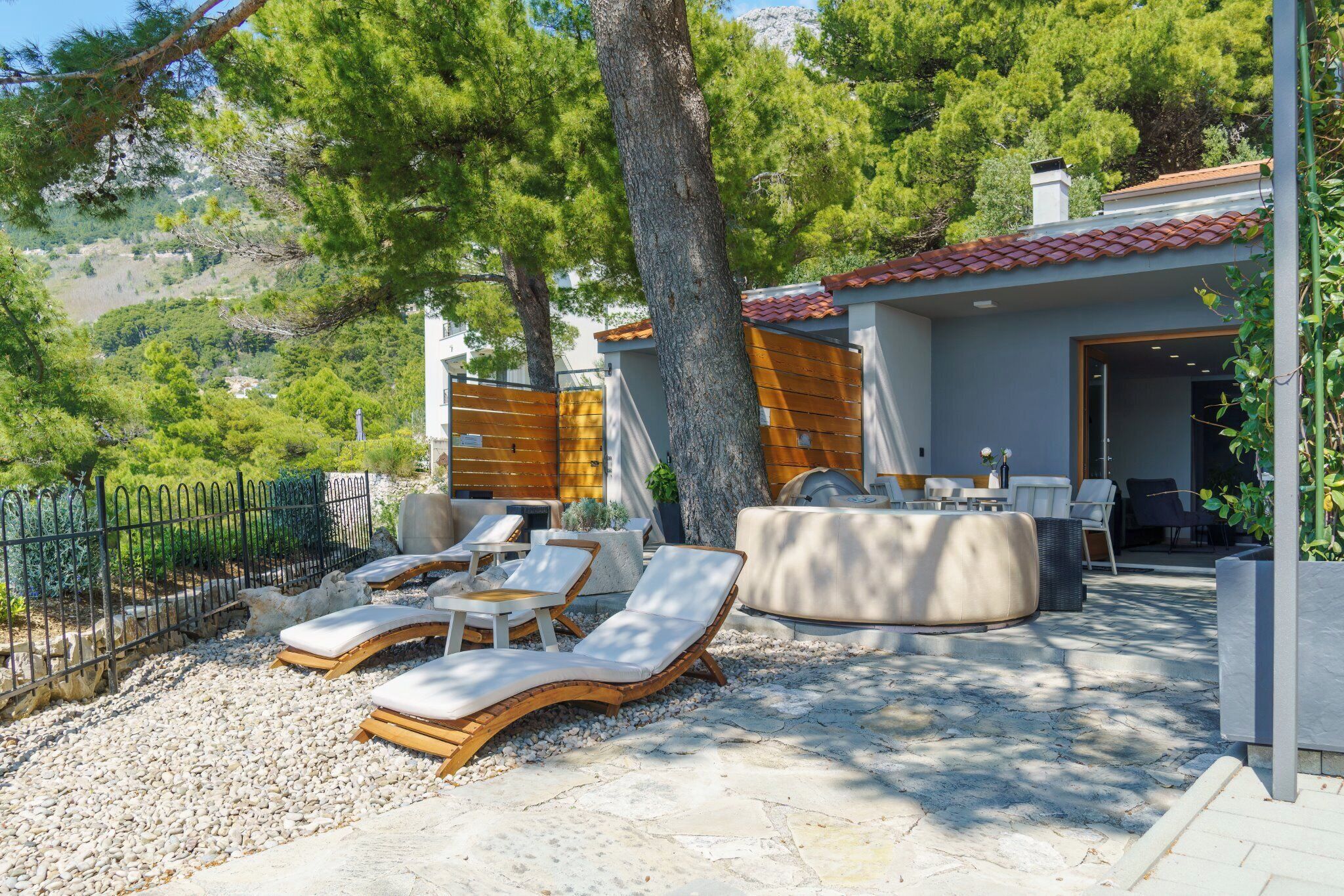 A patio area with sun loungers, a stone floor, and a view of a mountainous landscape.