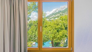 A room with a large window offering a view of a mountainous landscape and a body of water. - Apartments Bikin (Brela)