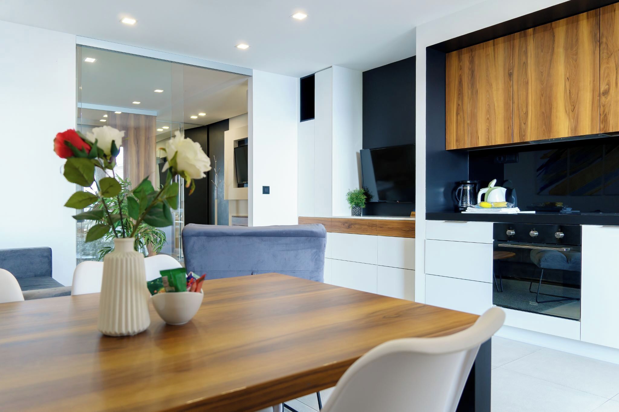 A modern kitchen with wooden cabinets, a built-in oven, and a dining area with a wooden table and white chairs.