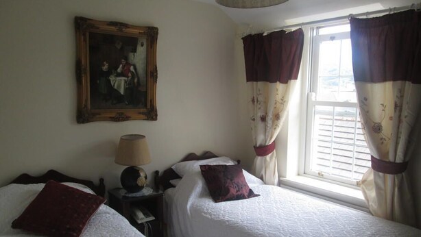 Un dormitorio con dos camas, una mesita de noche con lámpara, un cuadro en la pared y una ventana con cortinas.