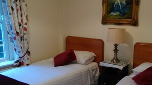 Habitación de hotel con dos camas individuales, una mesita de noche con lámpara, un cuadro en la pared y una ventana con cortinas.