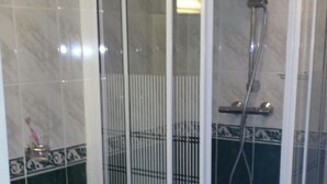 Un espacio de ducha con puerta de cristal, un cabezal de ducha y un accesorio de ducha manual.