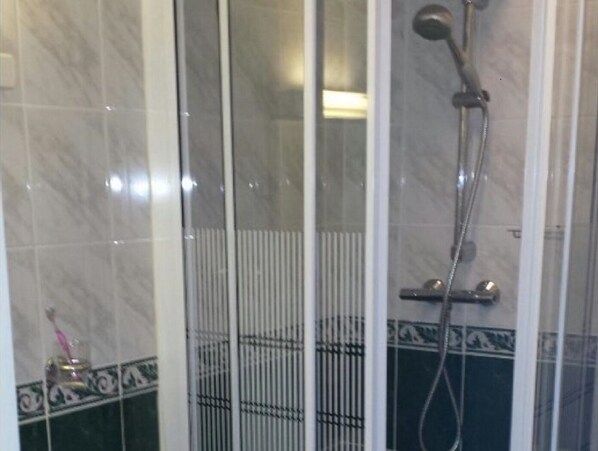 Un espacio de ducha con puerta de cristal, un cabezal de ducha y un accesorio de ducha manual.