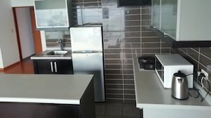 Una cocina moderna con un refrigerador de acero inoxidable, un lavamanos y una tetera sobre la encimera.