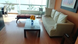 Una sala de estar moderna con un sofá, una mesa de centro con un jarrón de girasoles y vistas a palmeras a través de grandes ventanales.