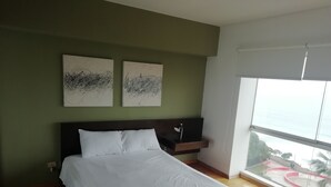 Un dormitorio con una cama grande, dos cuadros abstractos colgados en la pared, una mesita de noche con una lámpara y vistas a un parque a través de un ventanal amplio.