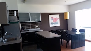 Una cocina moderna con comedor, que cuenta con una isla grande, muebles oscuros y una lámpara colgante.