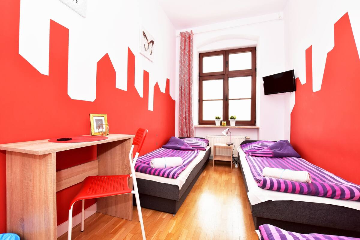 Une chambre avec deux lits, un bureau, une chaise, une télévision et une fenêtre avec des rideaux.