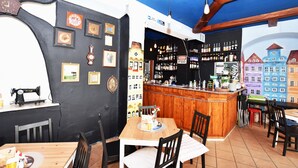 Un espace bar avec un comptoir en bois, des étagères remplies de bouteilles et une fresque murale représentant des bâtiments aux couleurs vives.