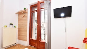 Une pièce avec une porte en bois, un radiateur, un téléviseur fixé au mur et une chaise rouge.