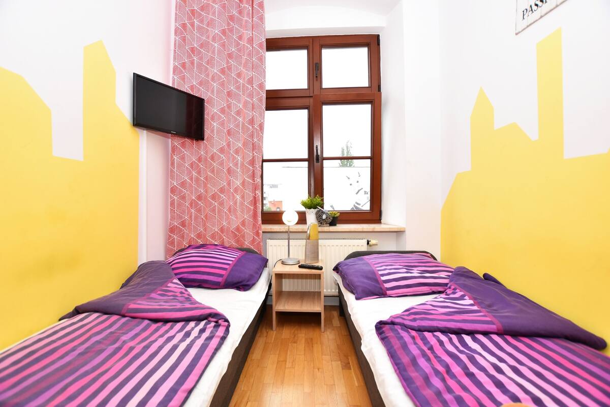 Une chambre avec deux lits, un téléviseur fixé au mur, une fenêtre donnant sur un beau paysage et une petite table avec une lampe.