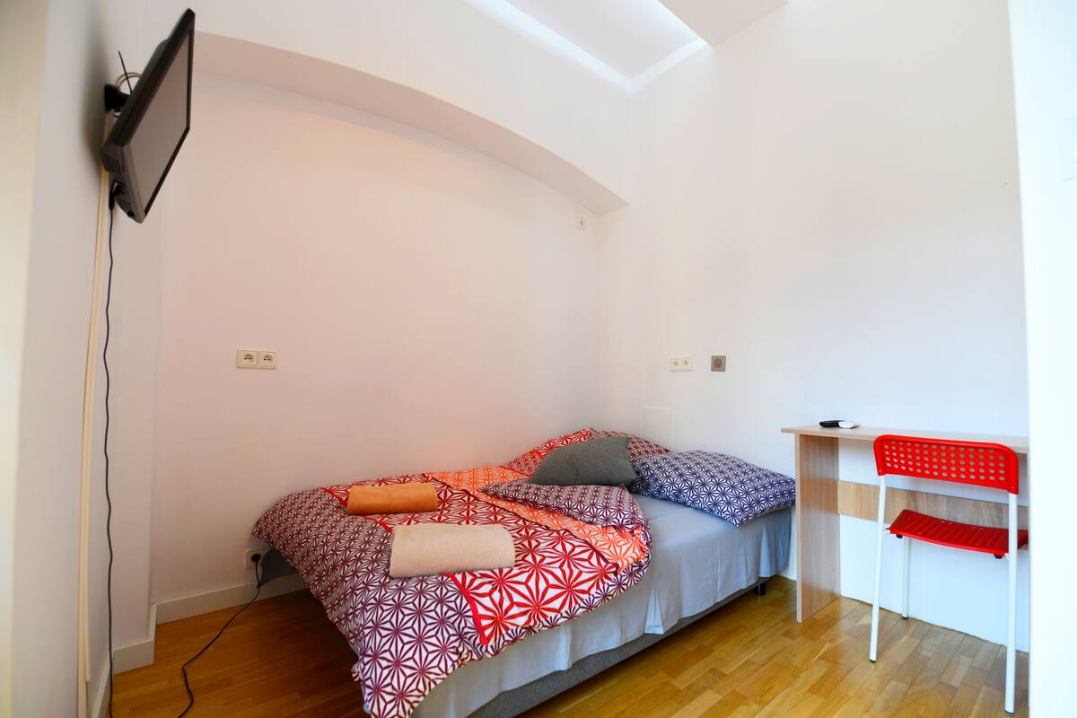 Une petite pièce bien éclairée, avec un lit, un bureau et une chaise.