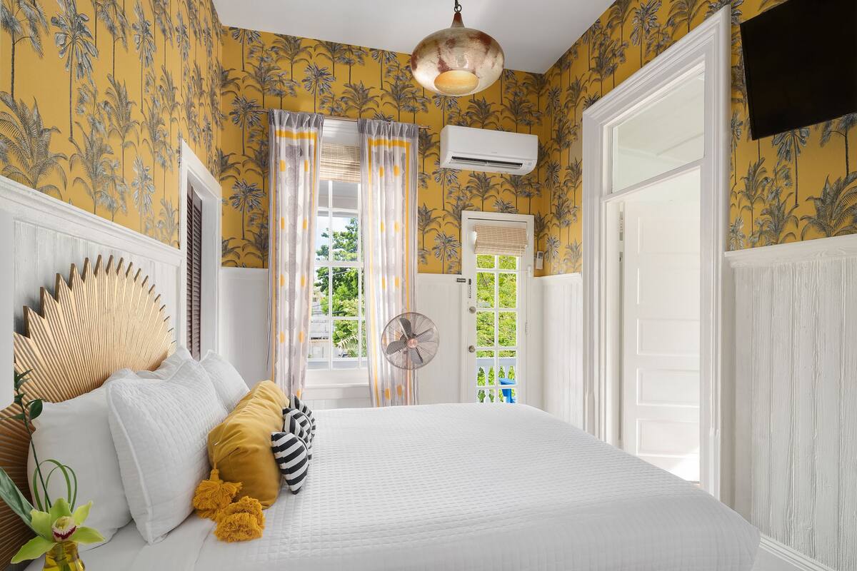 A bedroom with a bed, white bedding, a fan, and a window with curtains.