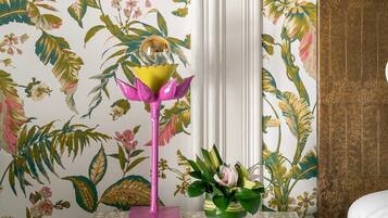 Una stanza con carta da parati floreale, un lampadario rosa e un vaso con piante verdi.