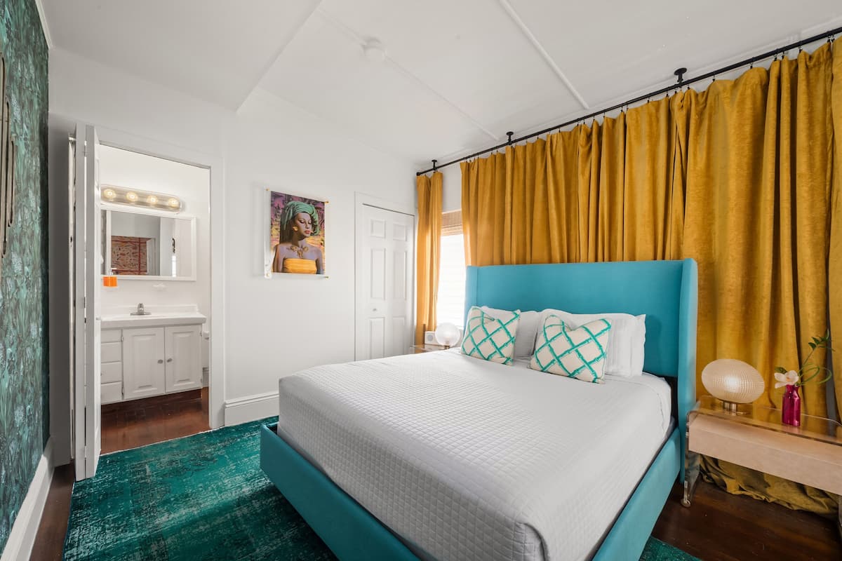 A bedroom with a bed, a vanity with a mirror, and a window with curtains.