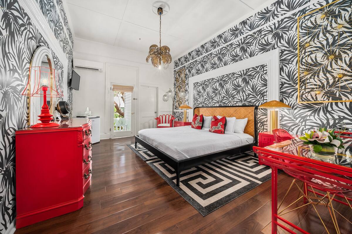 A bedroom with a bed, red dresser, and a red table with a vase.