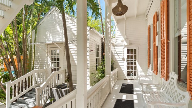 A covered porch with white railings, wooden benches, and a hanging light fixture. - Marrero's Guest Mansion (Key West)