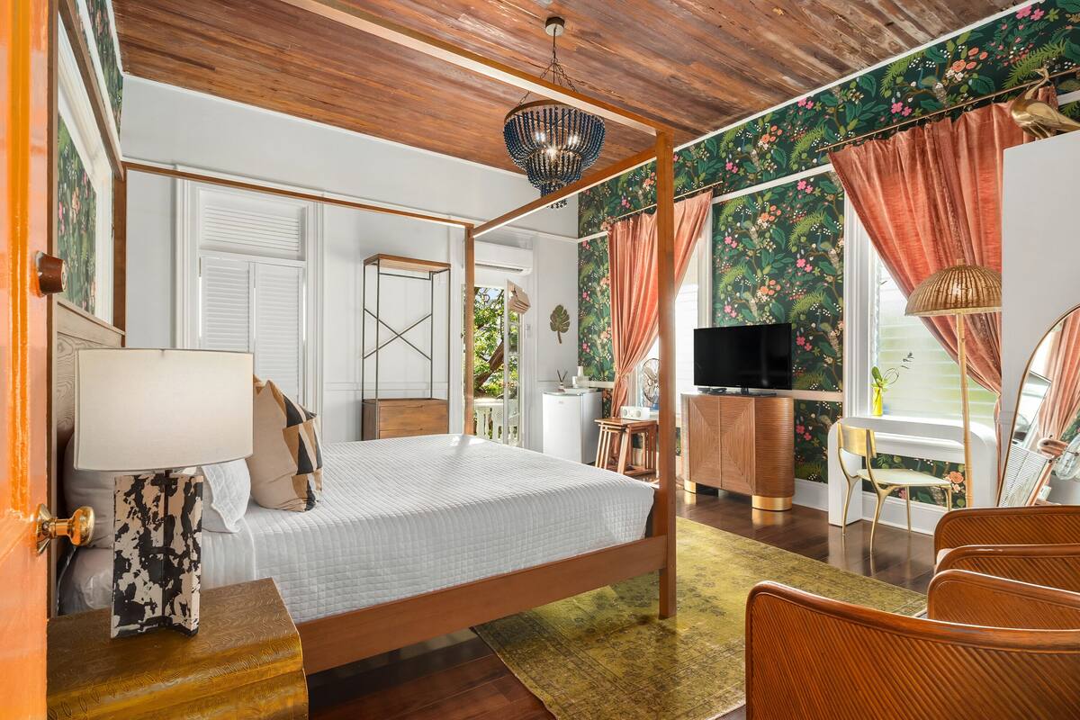 A bedroom with a four-poster bed, a television, a wooden cabinet, and a dining area with a table and chairs.
